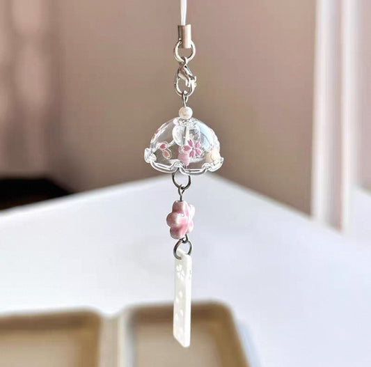 Decorative phone charm with a clear ball and pink flowers on a plain background